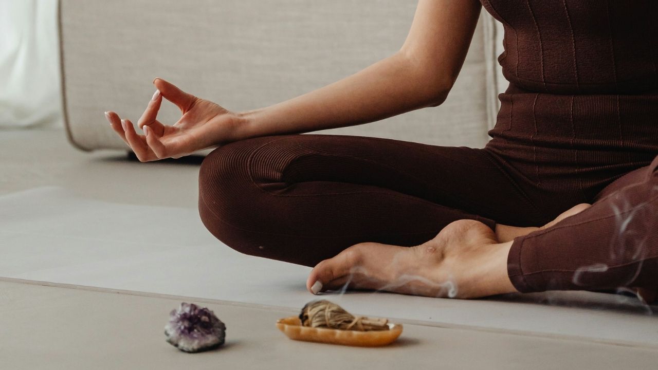 A person sitting cross-legged in a meditative pose, with crystals and burning sage placed in front, embodying mindfulness and peace.