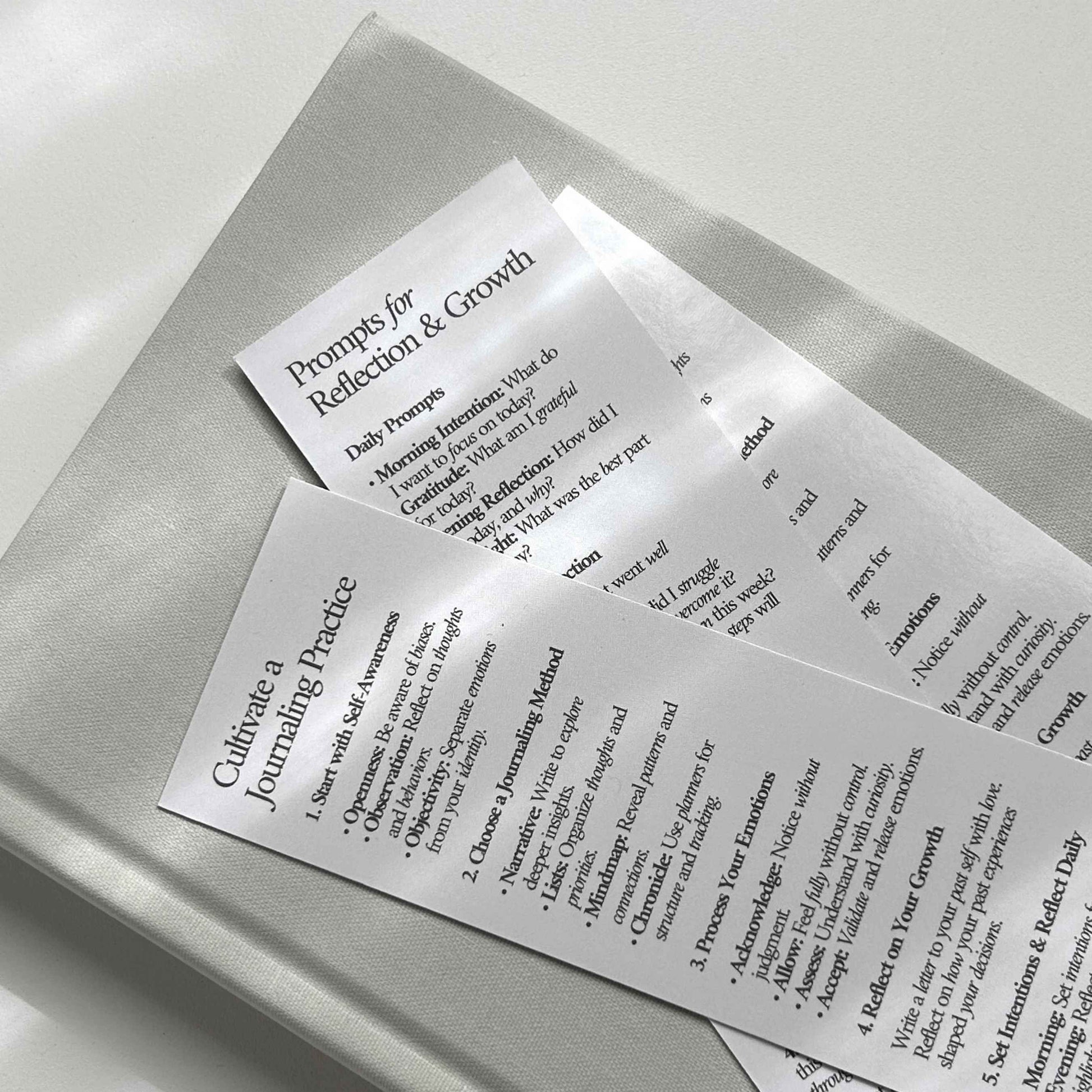 Close-up of journal bookmarks featuring 'Cultivate a Journaling Practice' and 'Prompts for Reflection & Growth,' with journaling prompts for daily reflection and self-awareness.